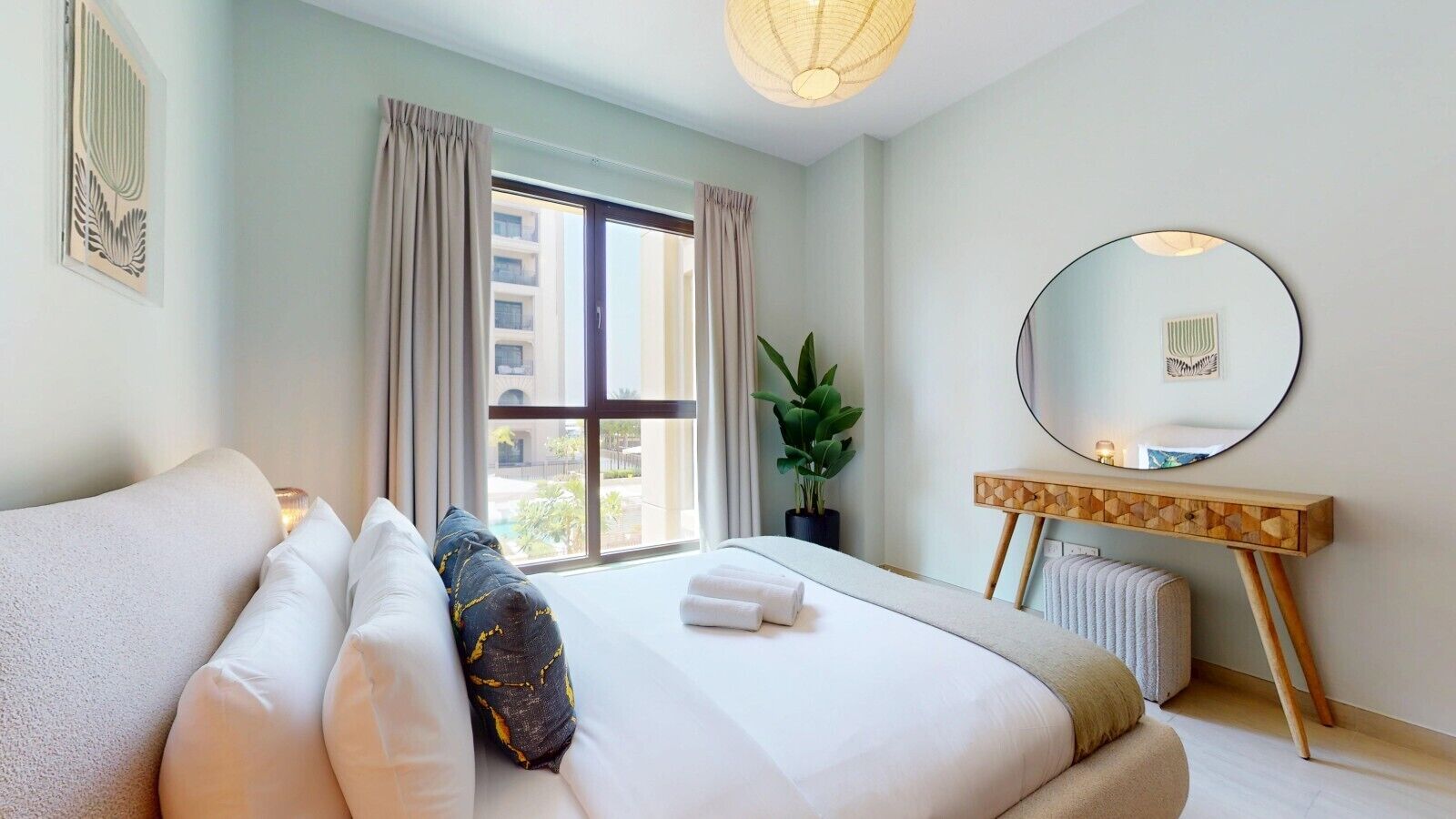 A hotel room with a large bed, a bedside table, a mirror, and a window with curtains.