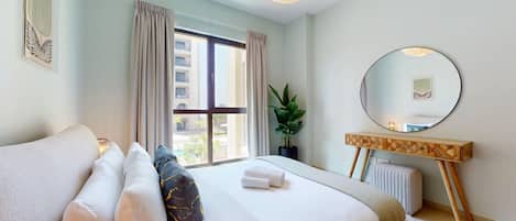 A hotel room with a large bed, a bedside table, a mirror, and a window with curtains.