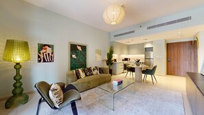 Ein modernes Wohnzimmer mit Sofa, Couchtisch und Lampe. Im Hintergrund ist eine Küchenzeile mit Esstisch und Stühlen zu sehen.