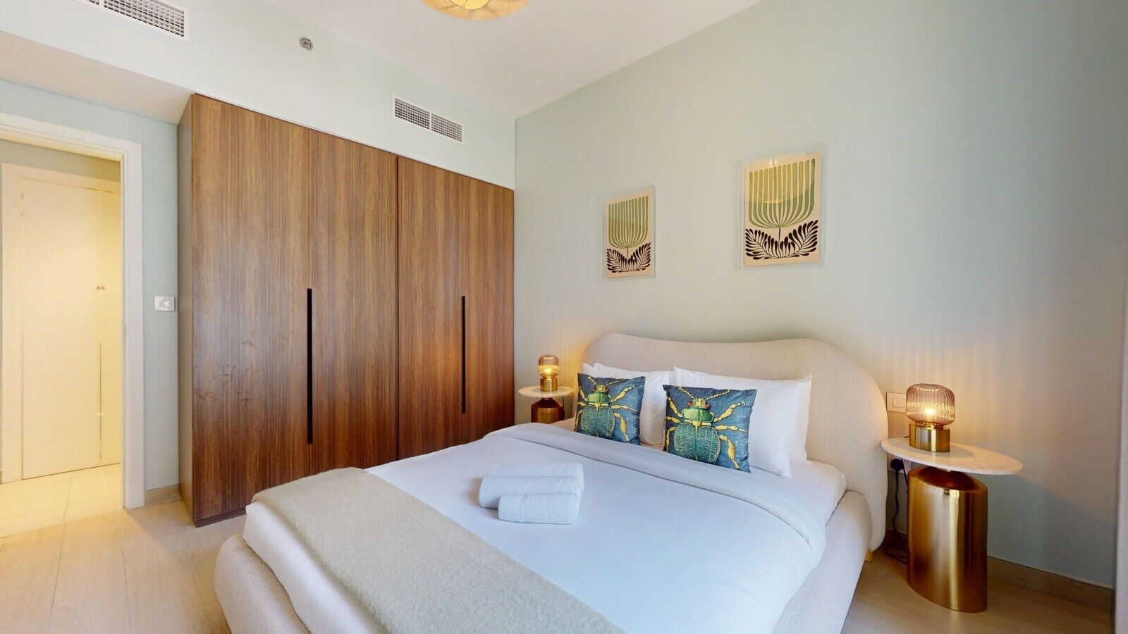 Ein Hotelzimmer mit einem großen Bett, einem Holzschrank, zwei Wandbildern, Nachttischlampen und einer Tür.
