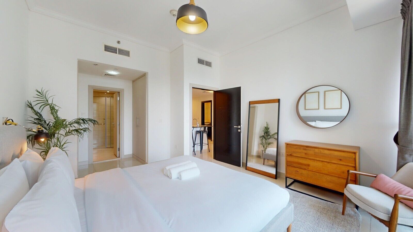 Une chambre d’hôtel avec un grand lit, une commode en bois, une chaise, un miroir et une plante en pot.