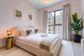 A hotel room with a large bed, a bedside lamp, a potted plant, and artwork on the wall. - Contemporary 1 Bed Near Burj Al Arab l Wild Wadi (Madinat Jumeirah Living)