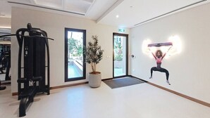 Ett gym med träningsutrustning, en krukväxt och en vägg med en illustration som visar en person som tränar.