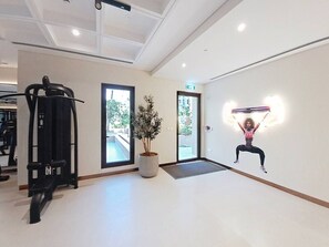 A gym with exercise equipment, a potted plant, and a wall with a fitness illustration. - Contemporary 1 Bed Near Burj Al Arab l Wild Wadi (Madinat Jumeirah Living)