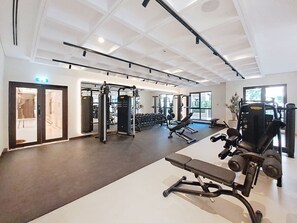 A gym with various exercise equipment, including benches and weight machines, and a large window providing natural light. - Contemporary 1 Bed Near Burj Al Arab l Wild Wadi (Madinat Jumeirah Living)