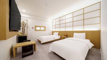 A hotel room with two beds, a TV, a wooden desk, and a bench.