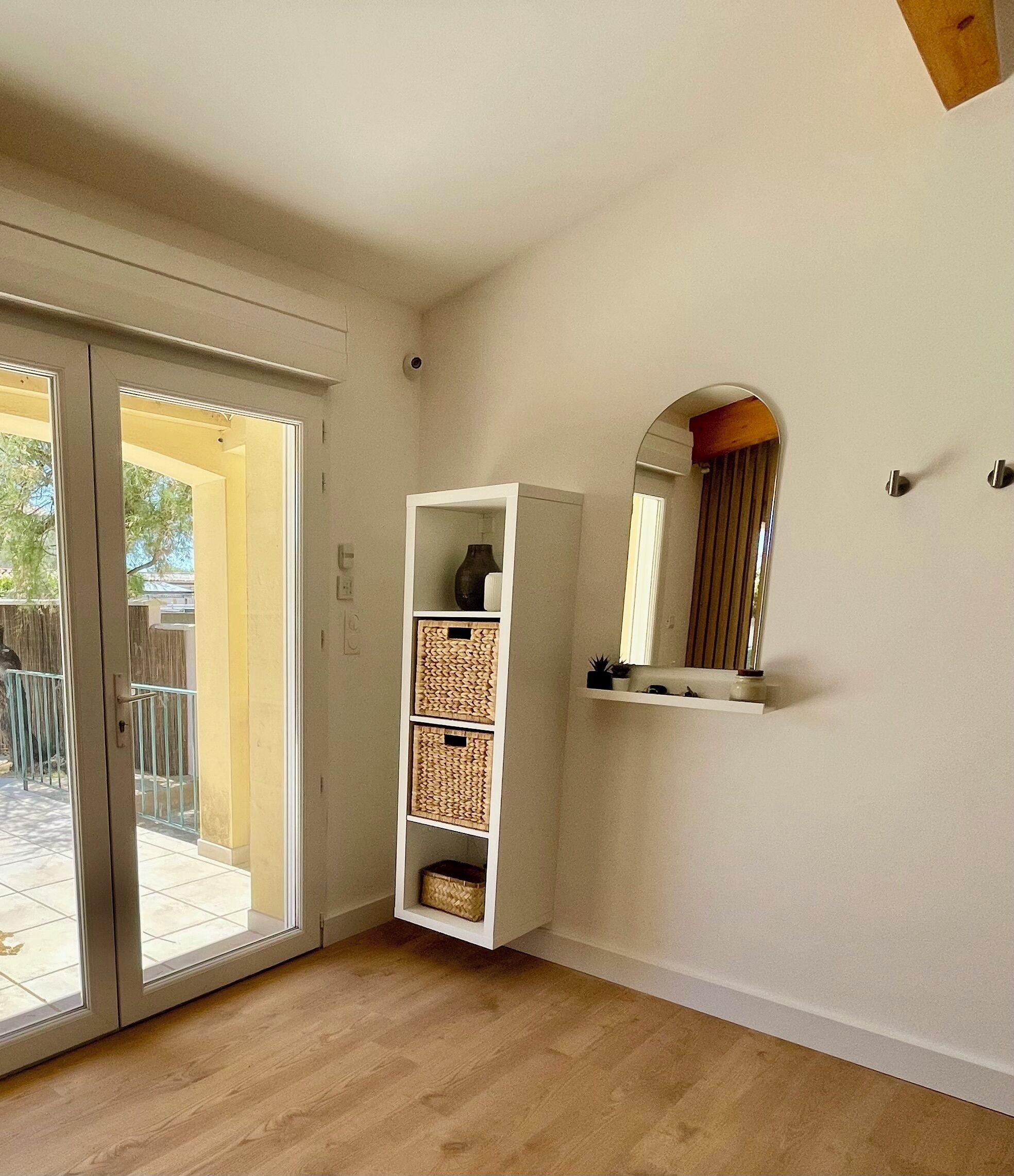 A room with a sliding glass door leading to an outdoor area, a white shelving unit with baskets, and a mirror on the wall.