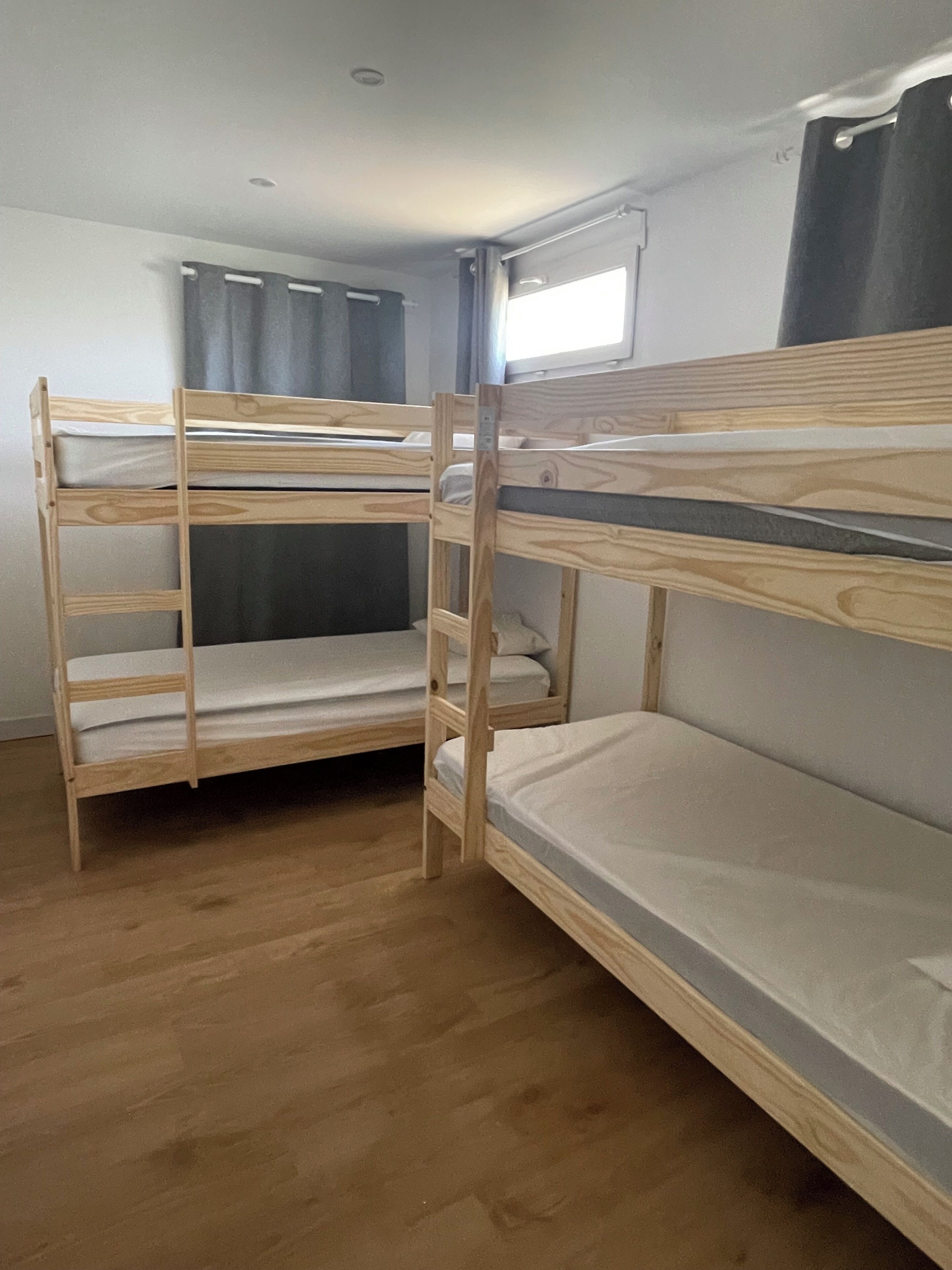A room with two bunk beds, a window with curtains, and a wooden floor.