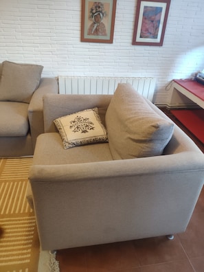 Ett vardagsrum med en beige soffa, en mönstrad prydnadskudde och ett element bakom soffan.