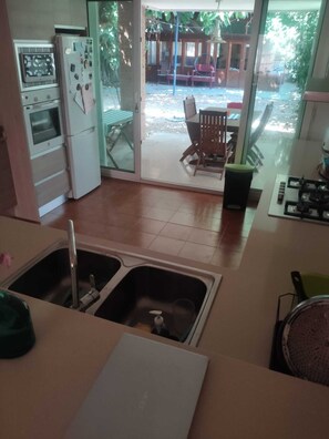 A kitchen with a double sink, a refrigerator, a stove, and a dining area with a table and chairs. - A unique house with a garden, very close to the beach (Playa de San Juan, Cabo Huertas)
