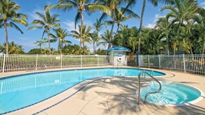 Ein Swimmingpool, umgeben von Palmen und einem weißen Zaun.