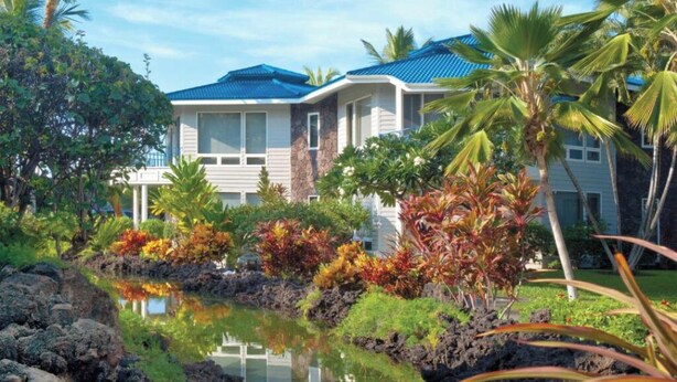 Ein Haus mit Pool, umgeben von tropischer Vegetation und blauem Himmel.