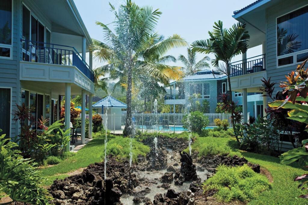 A hotel courtyard with a pool, palm trees, and a waterfall feature.