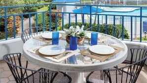Ein runder Tisch mit vier Stühlen, einer Glastischplatte und blauen Kerzenhaltern auf einem Balkon mit blauer Brüstung.