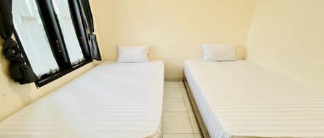 A small, single-room accommodation with two beds, a window with curtains, and a tiled floor.
