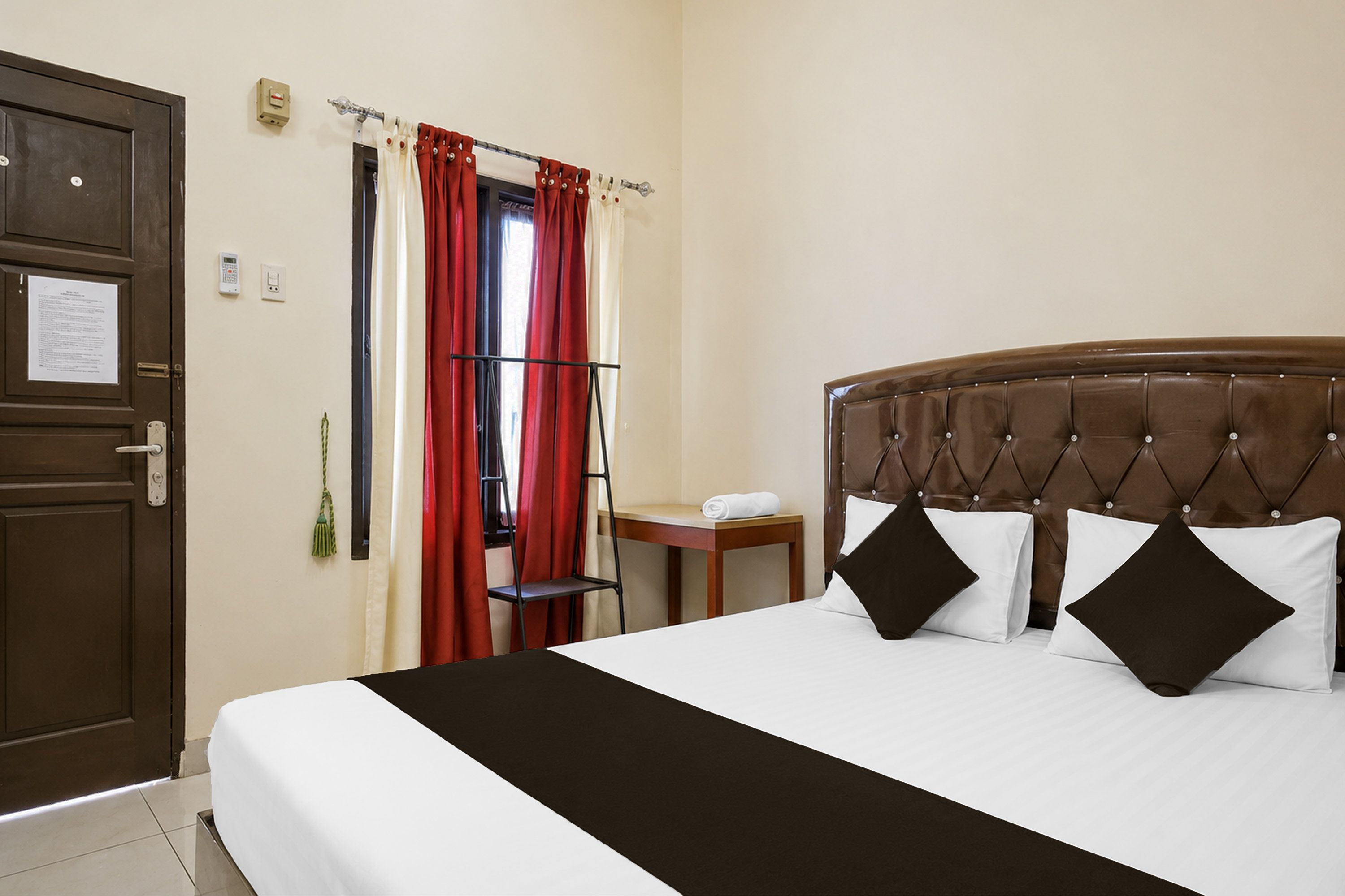 Une chambre d’hôtel avec un lit, une table de chevet, une porte et une fenêtre avec des rideaux.