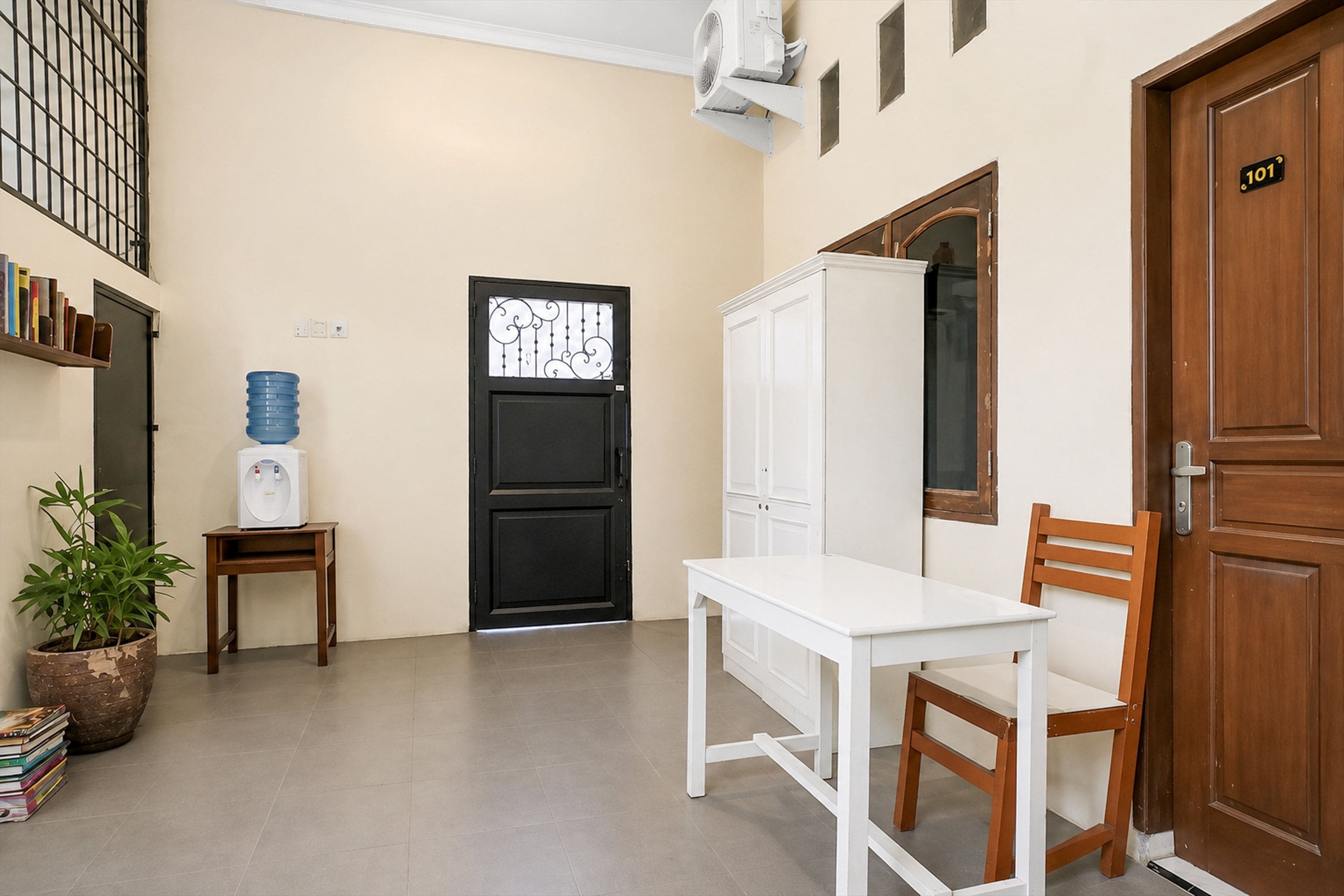 A room with a white table and chairs, a black door, a water dispenser, a bookshelf, and a potted plant.