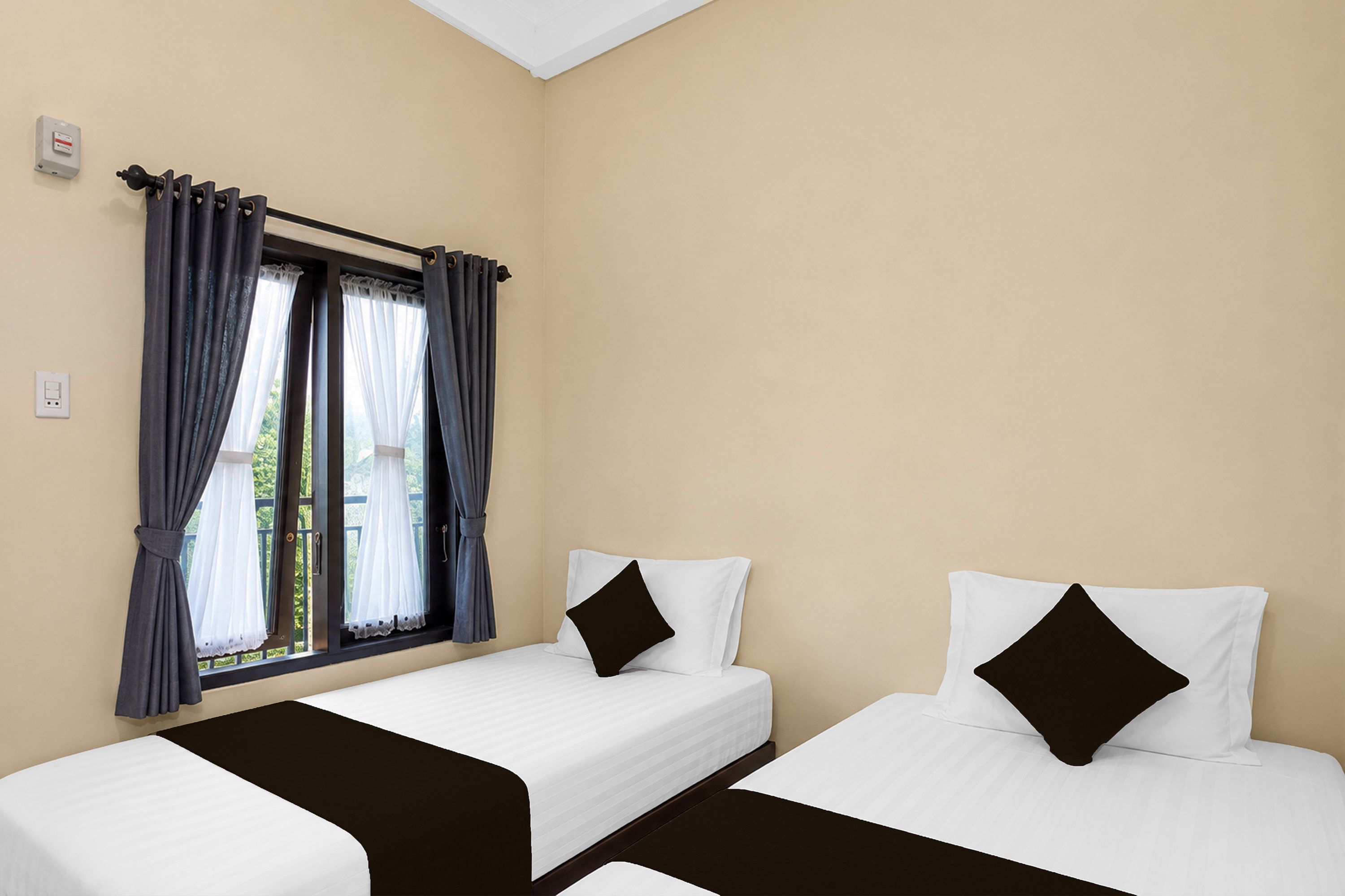 A hotel room with two single beds, a window with curtains, and a thermostat on the wall.