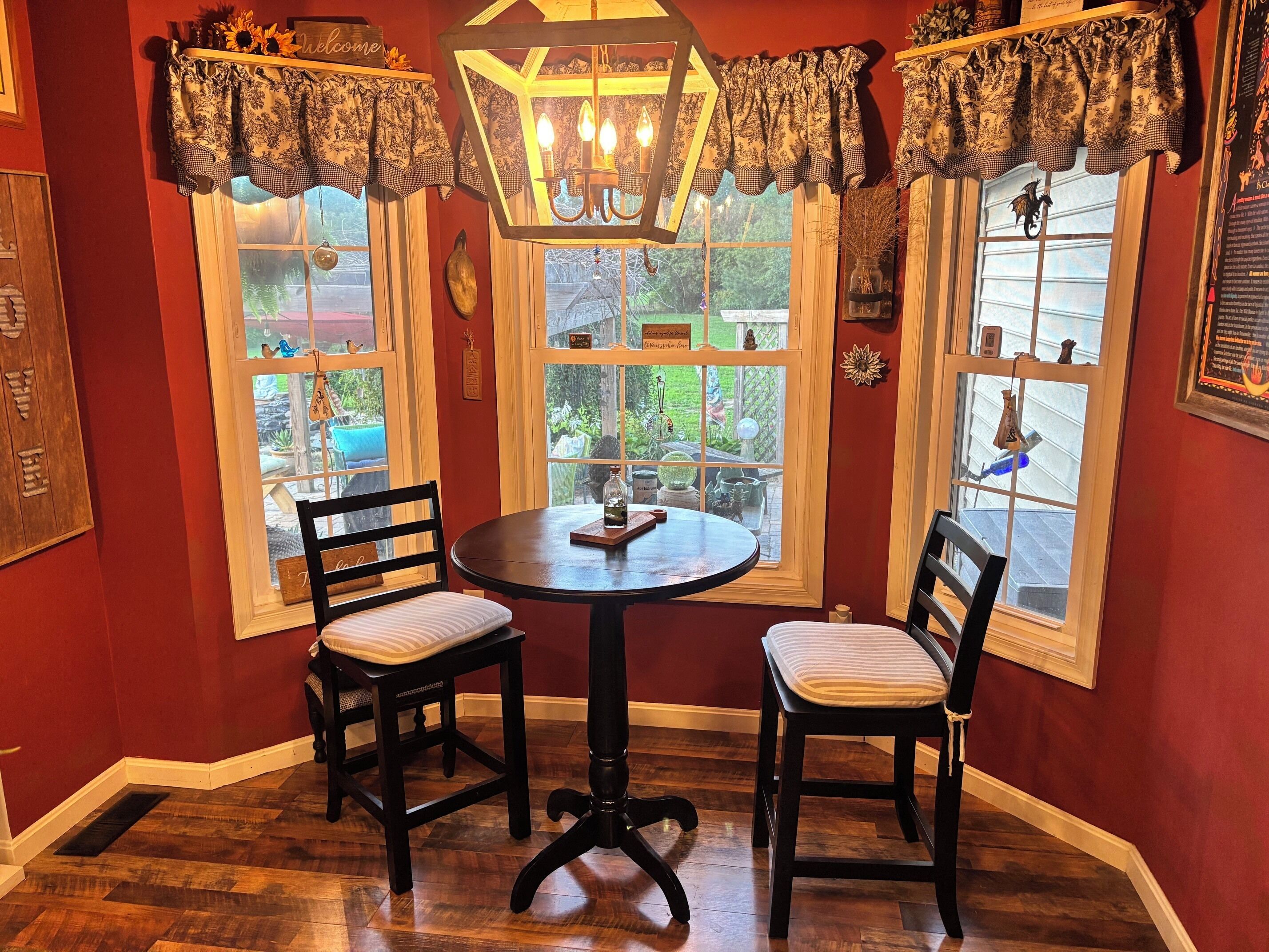 A cozy corner with a round table and two chairs, a chandelier, and a view of the outdoors through large windows.