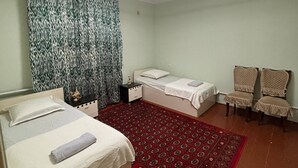 Een kamer met twee bedden, een rood tapijt met dessin, een plafondventilator en een gordijn met patroon.