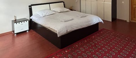 A bedroom with a bed, nightstand, wardrobe, and a red patterned rug.