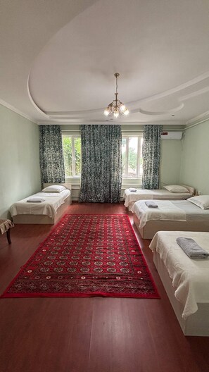 A hotel room with three beds, a red patterned rug, and a chandelier.