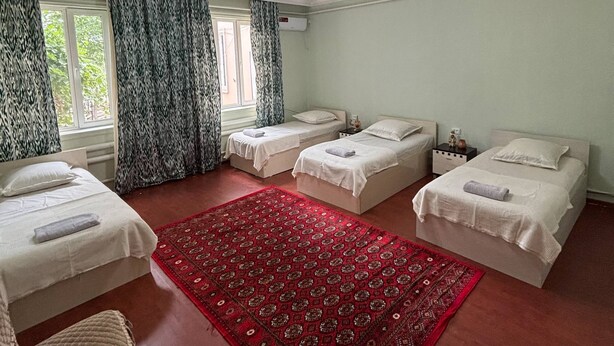 Een hotelkamer met drie bedden, een rood tapijt met dessin en een kroonluchter.