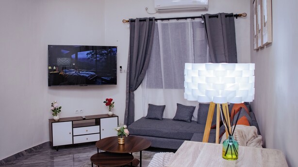 Una sala de estar moderna con televisor de pantalla plana, un sofá, una mesa de centro y una lámpara decorativa.