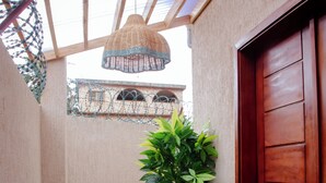 Pequeño espacio exterior amurallado con un banco de madera, una planta en maceta, una puerta y una lámpara colgante.