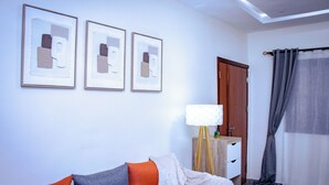 Una sala de estar con un sofá, una lámpara y tres obras de arte enmarcadas en la pared.