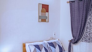 Un dormitorio con cama, mesita de noche con lámpara, aire acondicionado instalado en la pared y ventana con cortinas.