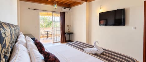 Habitación de hotel con cama, televisión, balcón con mesa y sillas, y un cisne decorativo sobre la cama.