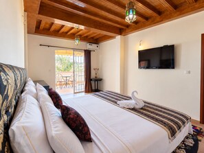 A hotel room with a bed, a TV, a balcony with a table and chairs, and a decorative swan on the bed. - Oasis de fes farm (Ain Bida)