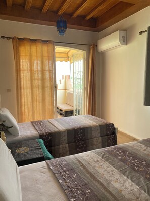 A room with two beds, a ceiling fan, an air conditioning unit, and a view of the outside.