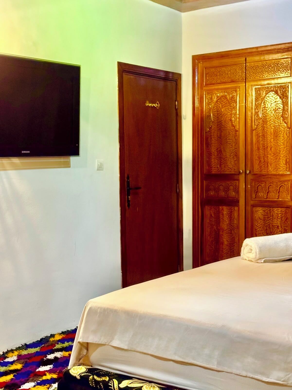 Un dormitorio con una cama, televisión montada en la pared y un armario de madera.
