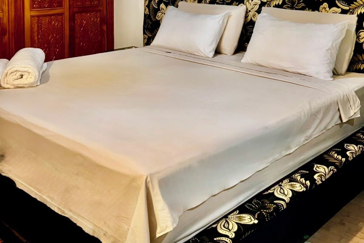 A hotel room with a bed, a wooden wardrobe, and a patterned headboard.