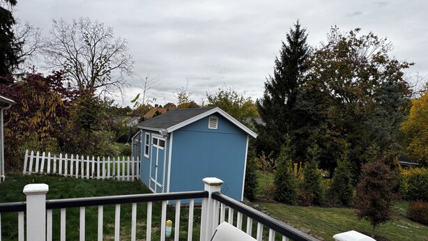 A blue shed, a white picket fence, and a glass table with a chair on a balcony.