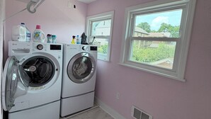 A laundry room with two front-loading washing machines, a drying rack, and a window providing a view of the outside.