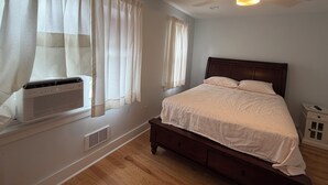 A bedroom with a bed, a window with curtains, a ceiling fan, and a small bedside table.