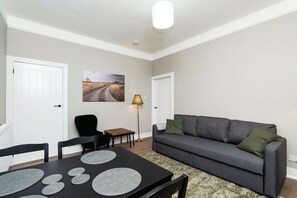 A living room with a grey sofa, a dining table with placemats, a lamp, and a painting on the wall. - Spacious Inverurie Stay -Nr Train Station -Parking (Aberdeenshire)