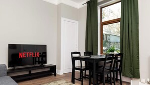 A living room with a television displaying 'NETFLIX,' a dining table with chairs, a sofa, and a window with curtains. - Spacious Inverurie Stay -Nr Train Station -Parking (Aberdeenshire)