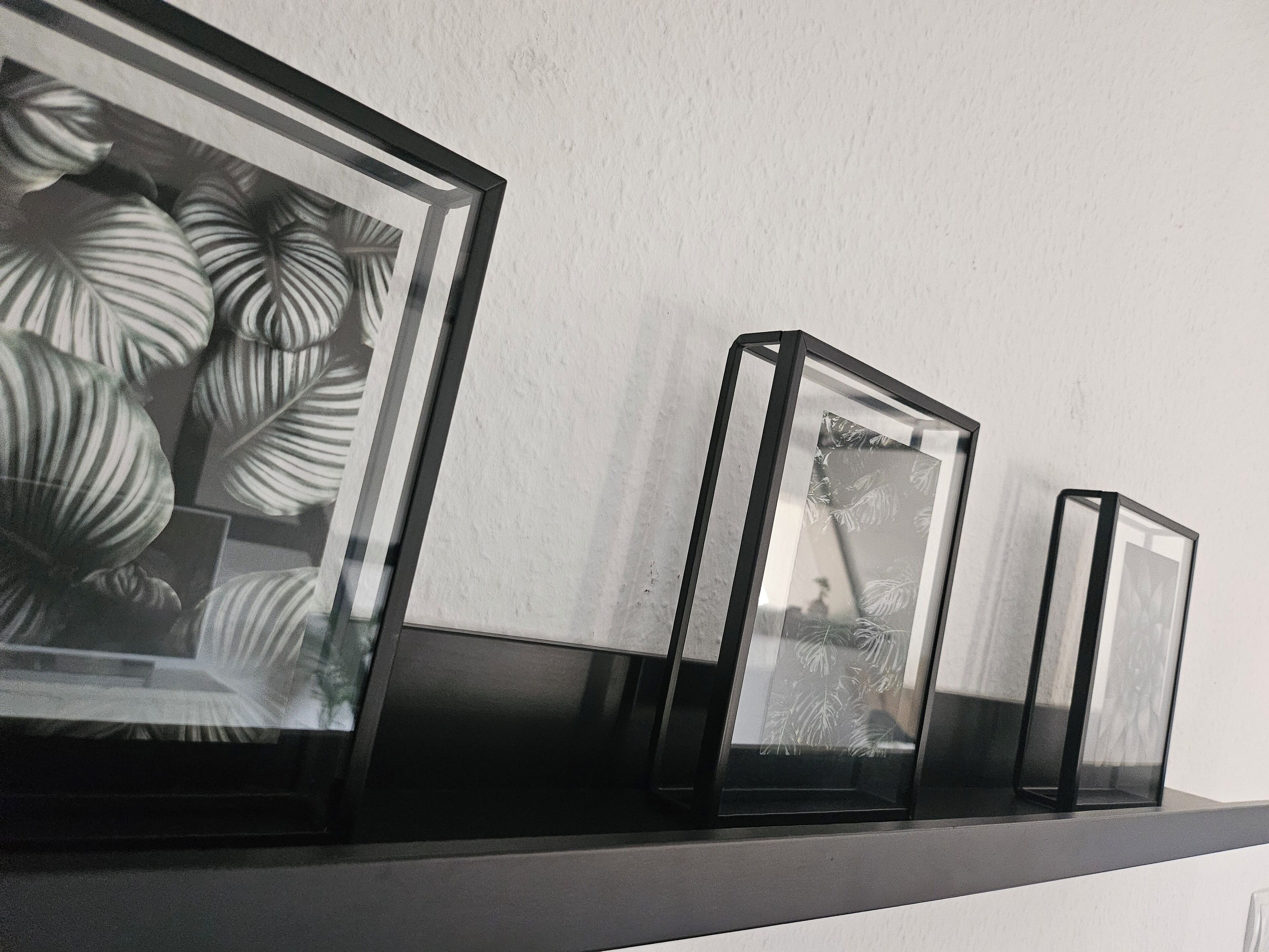 A series of black-framed glass objects on a shelf against a plain wall.