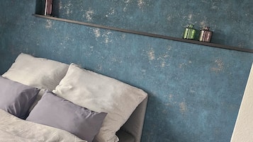 Ein Schlafzimmer mit einem Bett, Kissen, einem Nachttisch, einem kleinen Tisch und einem Regal mit Dekoration.