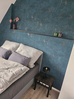 A bedroom with a bed, pillows, a nightstand, a small table, and a shelf with decorative items. - Modern vacation rental with a balcony, near the forest (Arnsberg)