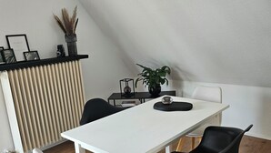 Een moderne eetruimte met een witte tafel, zwarte stoelen, een potplant en een radiator.
