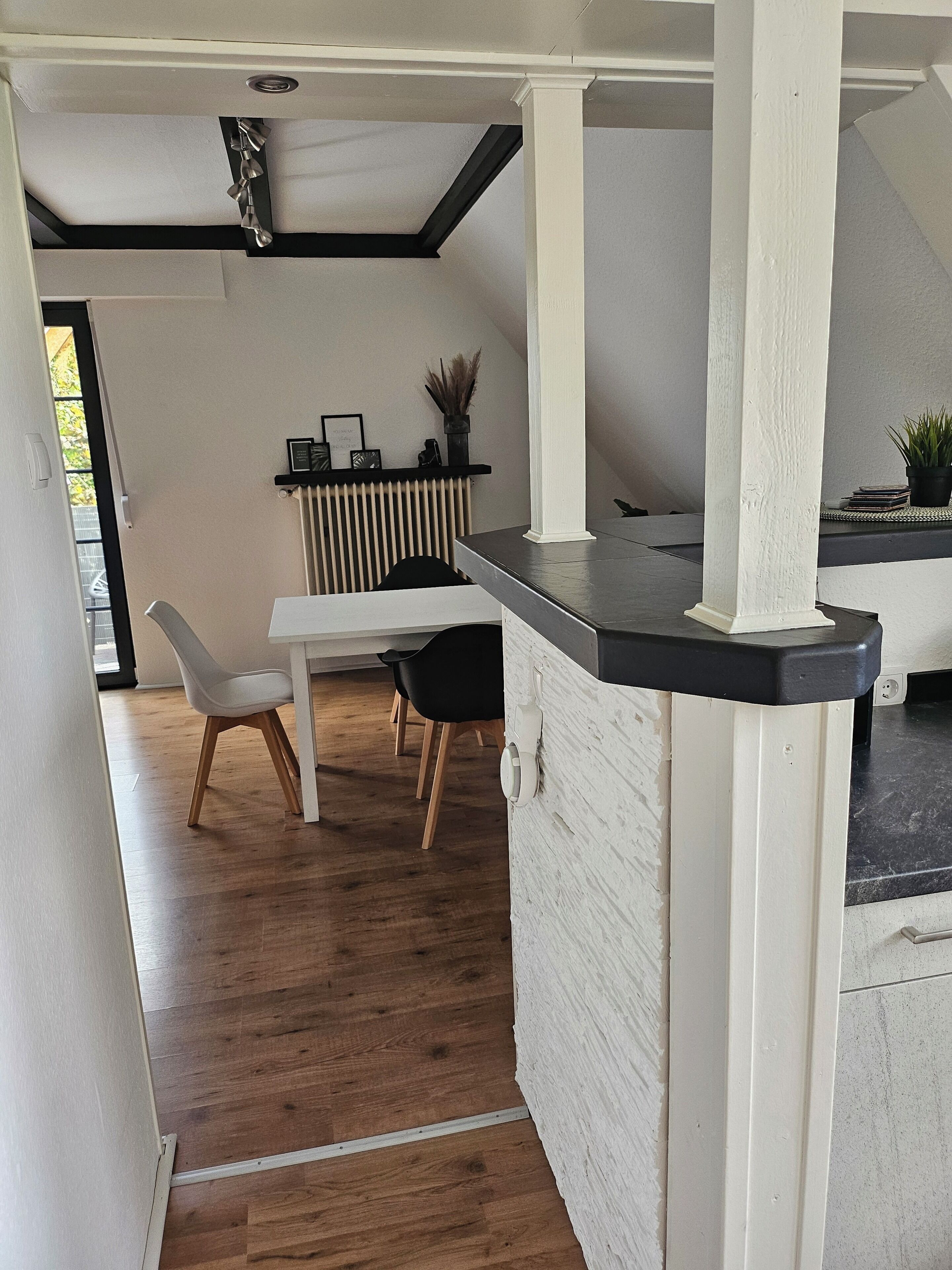Eine moderne Küche mit weißen Schränken, einer schwarzen Arbeitsplatte und einem Essbereich mit weißem Tisch und Stühlen.