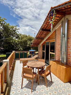 An outdoor patio with a round wooden table and chairs, a brick wall, and a pergola with hanging decorations. - Vrbo Property (Salvaterra)
