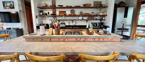 A kitchen with a central island, wooden chairs, and various kitchen items on shelves.