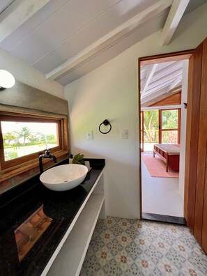 Une salle de bain avec un grand lavabo blanc, un meuble-lavabo en bois, une fenêtre et une porte donnant sur un balcon.