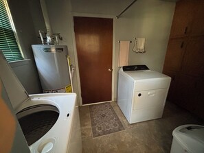 Une buanderie équipée d’un lave-linge et d’un sèche-linge, d’un chauffe-eau et d’une porte donnant sur une autre pièce.